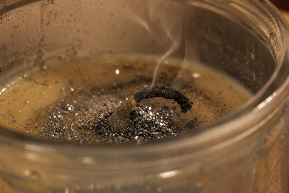 Taittunut hiiltynyt sydänlanka kuorrutettuna kasautuneella hopeisella glitterillä jähmettyneessä vahassa, kynttilä on sammunut.
